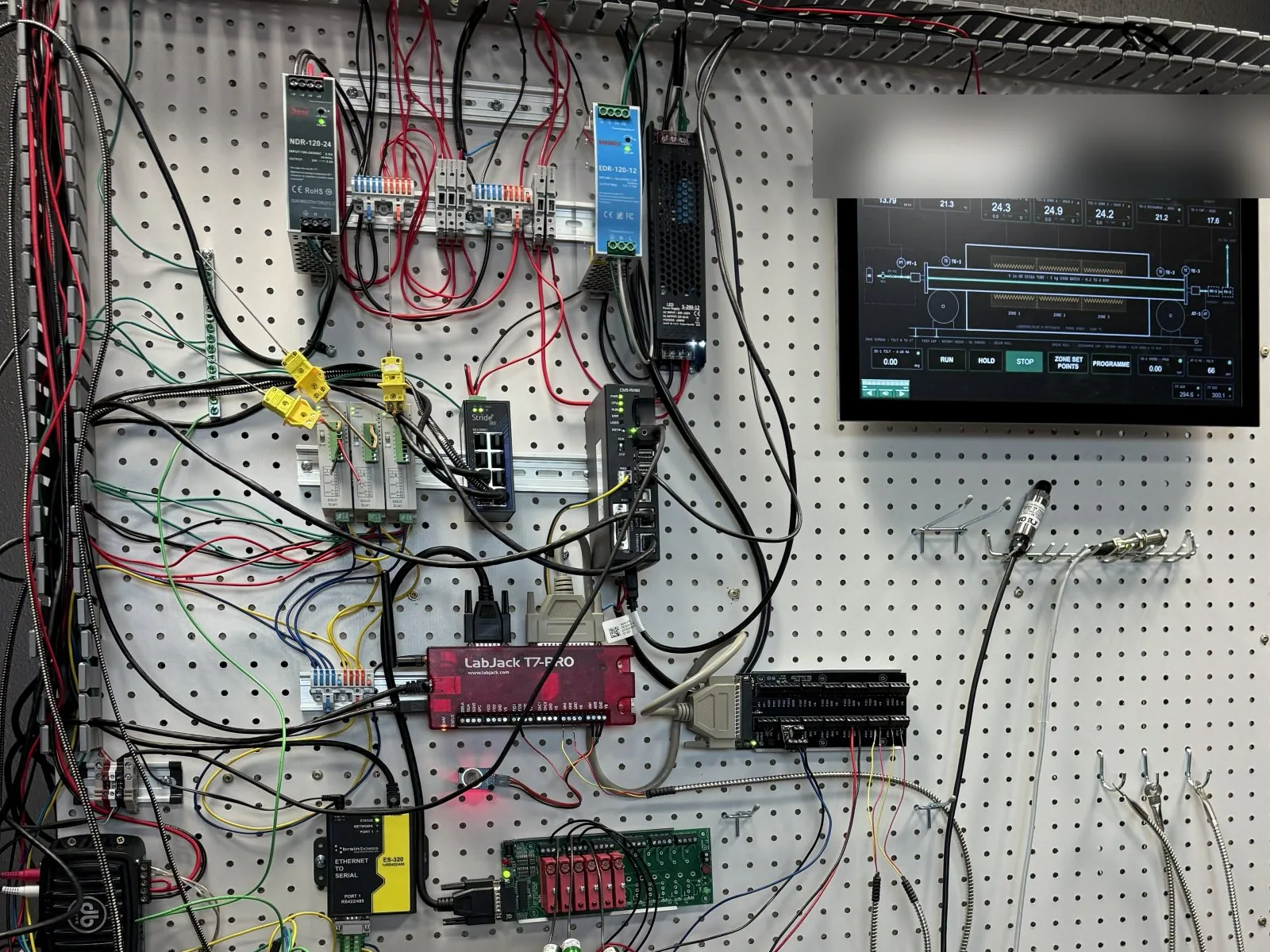 Control panel for a rotary kiln on white pegboard, with power supplies, temperature controllers, a data-acquisition unit and a touchscreen operator panel