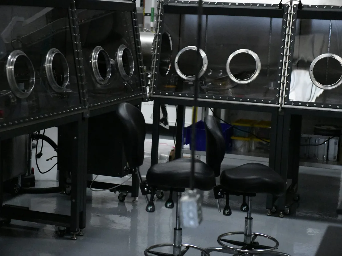 Row of glovebox ports with gloves hanging inside, a stool in front