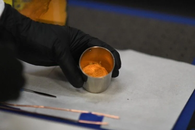 Gloved hand holding a small cup of orange-yellow yellowcake powder